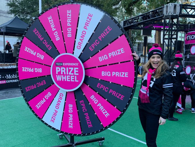 Person standing next to a large prize wheel with 'BIG PRIZE' and 'EPIC PRIZE' text on a green surface.